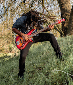 Headbanging dreadlocks on a grassy hill play a cherry sunburst pedulla bass guitar