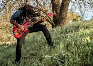 Headbanging with dreadlocks on a grassy hill playing a red bass guitar