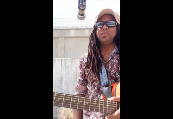 Brian with sunglasses and a had wearing an acoustic guitar dreadlocks hanging down